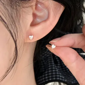 Minimalist sterling silver heart stud earrings for women shown as worn on ear close-up