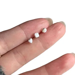 Set of minimalist silver heart and geometric stud earrings shown on fingers for scale