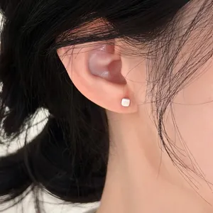 Macro view of a minimalist square silver stud earring worn elegantly on a female ear