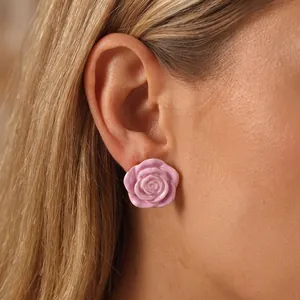Detail shot of a pink rose enamel earring with gold-plated edges on a model's ear.