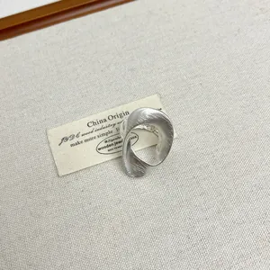 Close-up van mat zilveren ovale holle ring met geborstelde textuur op beige stof