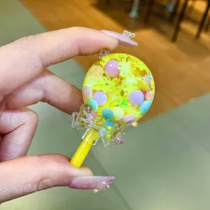 Close-up of a lollipop-shaped oil shaker charm with yellow glitter and colorful beads.