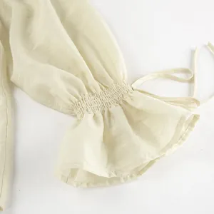 Detailansicht eines eleganten Rüschenärmels mit Smok und zarten Bändern an beiger Bluse