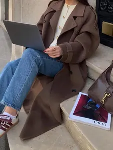 Detail shot of a chic brown double-breasted long overcoat for women's autumn office wear.