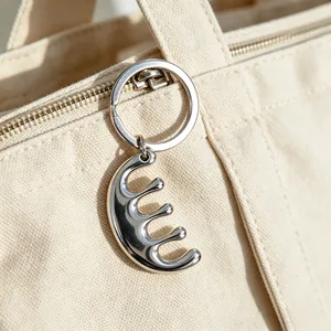 Close-up of a minimalist silver stainless steel comb keychain hanging on a canvas bag