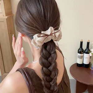 Detailed view of a beige polka dot scrunchie with a brown bow on a braided hairstyle