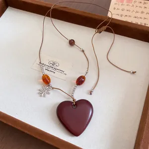 Détail du collier pendentif cœur avec perles en bois et fleur argentée sur cordon.