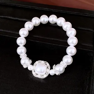 Primer plano de pulsera elástica de perlas blancas con adorno central de plata y circón.