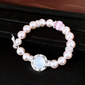 Vista detallada de una pulsera de perlas rosas con un acento central de piedra blanca.