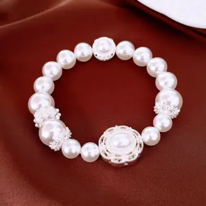 Elegante pulsera de perlas blancas con dijes huecos plateados y circonitas sobre seda