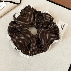 Close-up of brown polka dot scrunchie with white ruffled edges and gold charm.