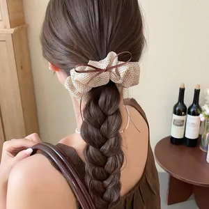 Detailed view of a vintage cream polka dot scrunchie with a brown bow on a braided ponytail.