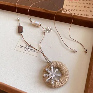 Détail du pendentif en jute avec fleur argentée sur un cordon perlé de style chinois
