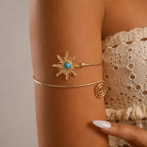 Detailopname van een vintage gouden zon-armring met turquoise steen op de arm van model