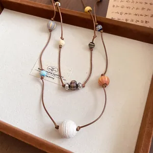 Détail d'un collier à double cordon en cuir orné de diverses perles en bois colorées.