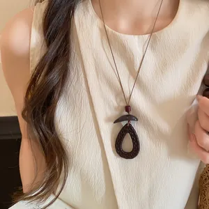 Détail d'un long collier en bois avec pendentif sombre et cordon en cuir marron