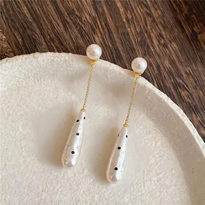 Detailed macro view of elegant teardrop pearl drop earrings with black polka dots and gold chain
