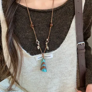 Détail d'un long collier en cuir bohème avec des perles de bois et un pendentif turquoise