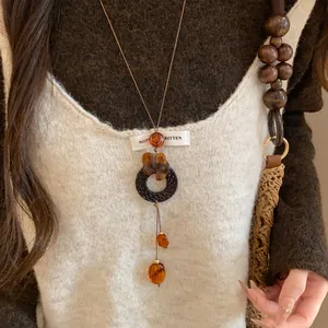 Vue détaillée d'un collier long avec perles de résine ambrée et anneau tressé noir.
