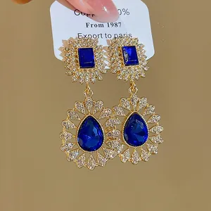 Close-up of vintage royal gold earrings with blue teardrop crystals and pavé rhinestones.