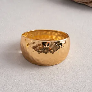 Close-up detail of a bold gold metal bangle featuring a unique hammered texture.