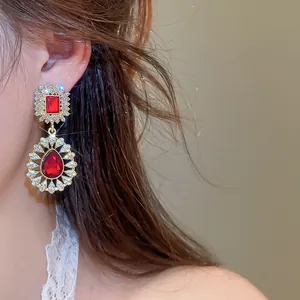 Detailed view of retro court style earrings with red teardrop crystals on a model.