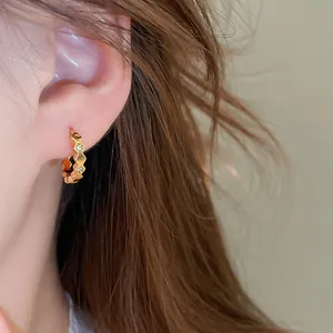 Close-up detail of a minimalist 18k gold plated huggie earring with zircon stones.