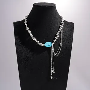 Detailweergave van zilveren kralenketting met maan- en ster-kwastjes en blauwe steen
