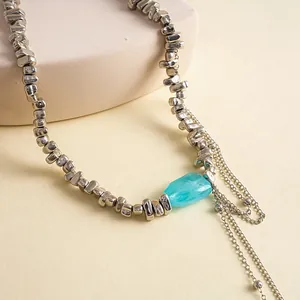 Detailopname van een zilveren ketting met geometrische kralen en een helderblauwe edelsteen