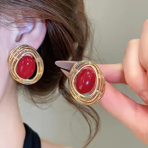 Nahaufnahme von goldenen ovalen Vintage-Ohrsteckern mit rotem Harzstein-Detail.
