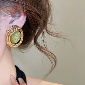 Nahaufnahme von Vintage-Ohrstecker, oval und hohl, mit einem grünen Harzstein.