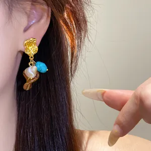 Close-up view of vintage gold drop earrings with turquoise and resin stones on model