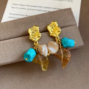Detail view of retro stud earrings featuring turquoise stones and amber resin leaf pendants