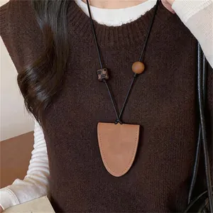 Detailopname van een vintage halsketting met bruine leren hanger op een donkere trui.