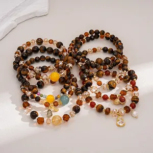Detail view of layered tiger eye and glass beaded bracelets with charms and warm tones.