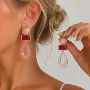 Vista detallada de pendientes geométricos de acrílico en tonos rosa y magenta en modelo.