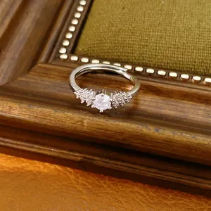Detail view of an elegant open ring featuring a sparkling central zircon on a wooden frame.