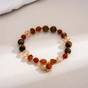 Vintage tiger eye stone beaded bracelet with a gold acorn charm on textured background