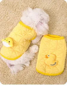 Detail view of a yellow quilted puppy vest featuring a cute plush duck ornament on carpet