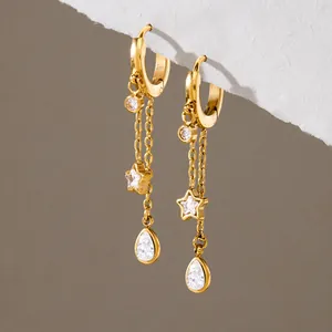 Close-up of gold stainless steel hoop earrings with star and teardrop tassel charms