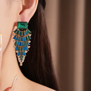 Detaillierte Nahaufnahme von grün-blauen Strass-Kronleuchter-Ohrringen getragen von einem Modell