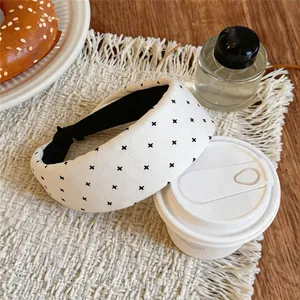 Detail view of a white fabric headband with black cross patterns on a woven mat