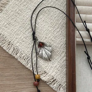 Detalle de collar vintage con colgante de hoja de plata, cordón negro y cuentas de colores