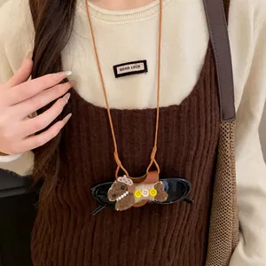 Gros plan d'un collier pince à lunettes petit chien en cuir marron sur le modèle.