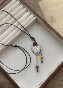 Vista detallada de un collar con colgante de hoja y cuentas de cerámica de colores en cordón