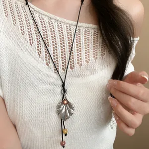 Detalle de un collar con colgante de hoja plateada y cordón de cuero en una blusa.