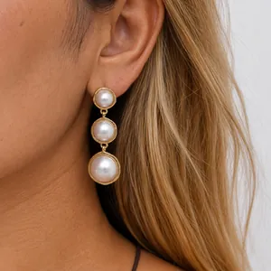Close-up of elegant gold triple pearl dangle earrings on a model's ear