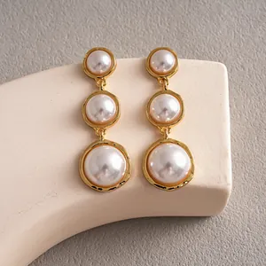 Macro detail of vintage gold drop earrings featuring three graduated circular pearls.
