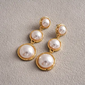 Detail view of elegant gold metal drop earrings with three graduated pearls on textured background