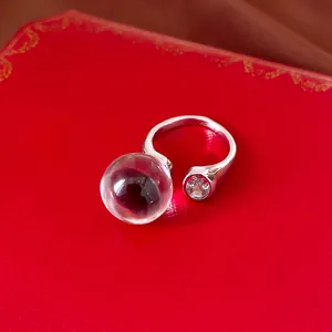 Nahaufnahme eines silbernen Rings mit einer klaren Harzkugel und einem funkelnden Zirkon